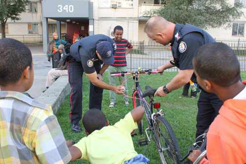Division Somali Liaison unit officers P.C. Ammar Khan, left, and Sgt. Chris Laush, right, spray painting bikes with children in the courtyard of Kingsview Village high-rise apartment complex on Dixon Rd.(Dixon community: 320, 330, 340 Dixon Rd.)